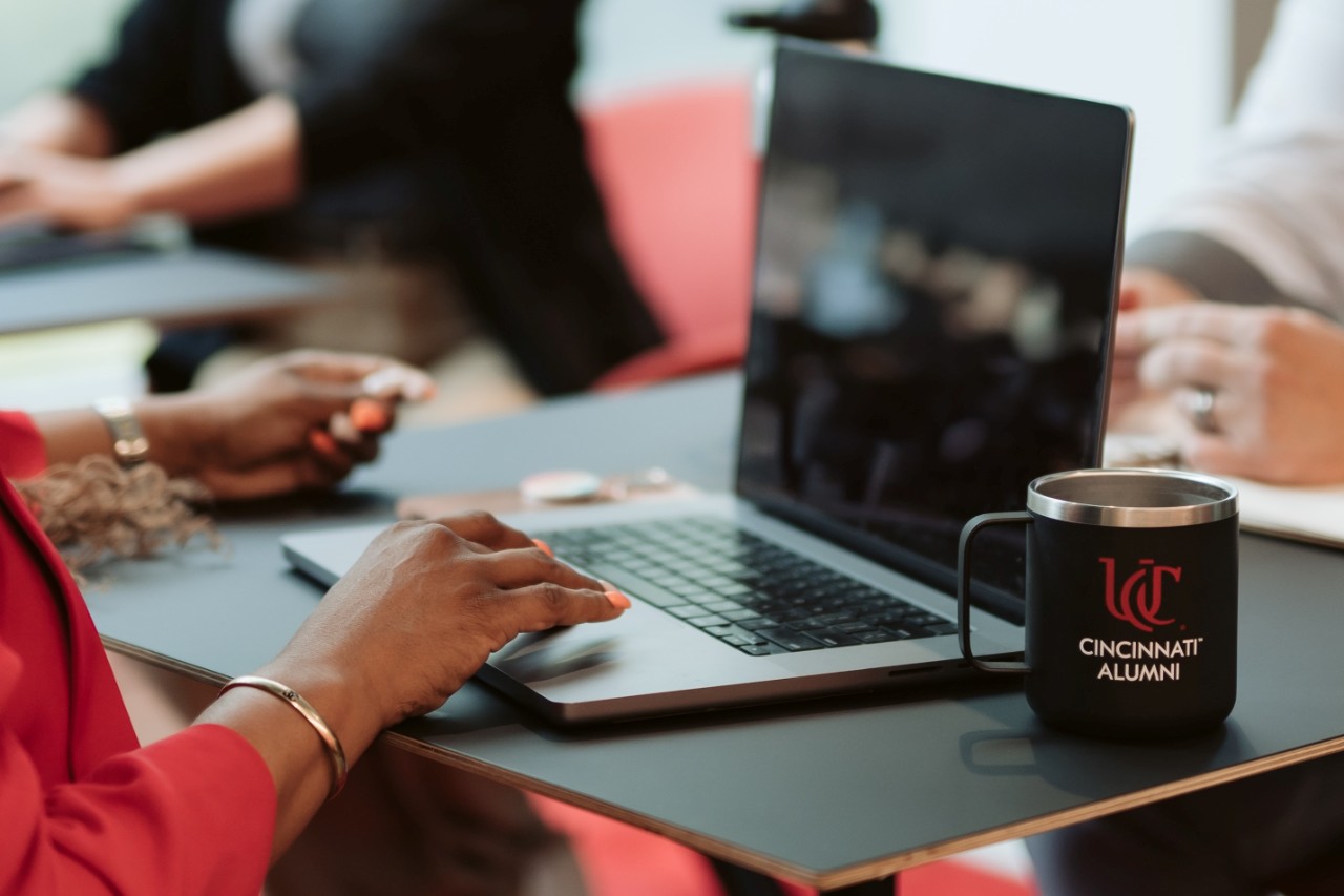 Woman typing on a laptop with a UC Cincinnati Alumni coffee mug next to her