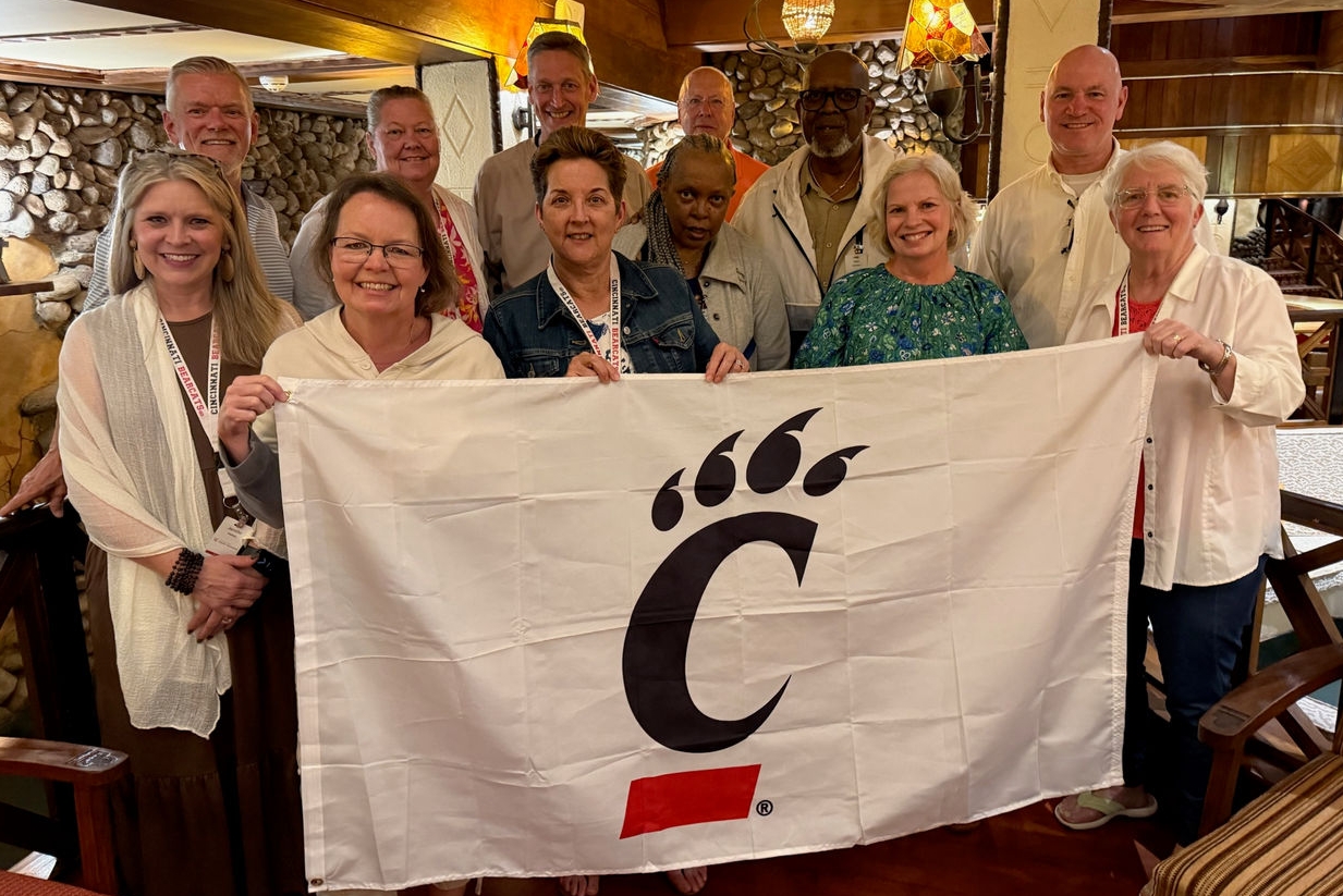 Group of UC alumni holding a C-paw flag on a trip to Tanzania