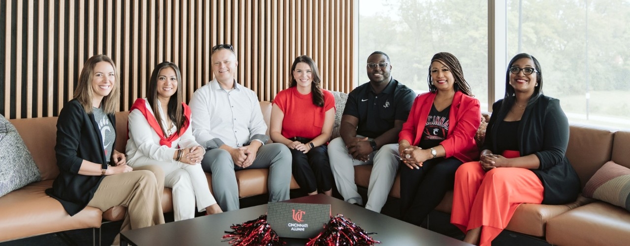 A group of alumni smiling while sitting on a couch