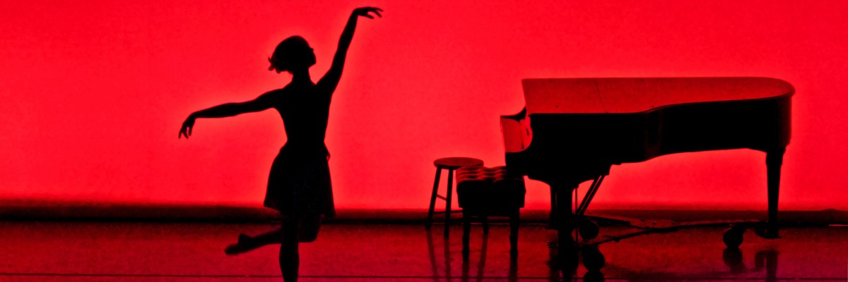 ballerina posing next to a piano with a red background