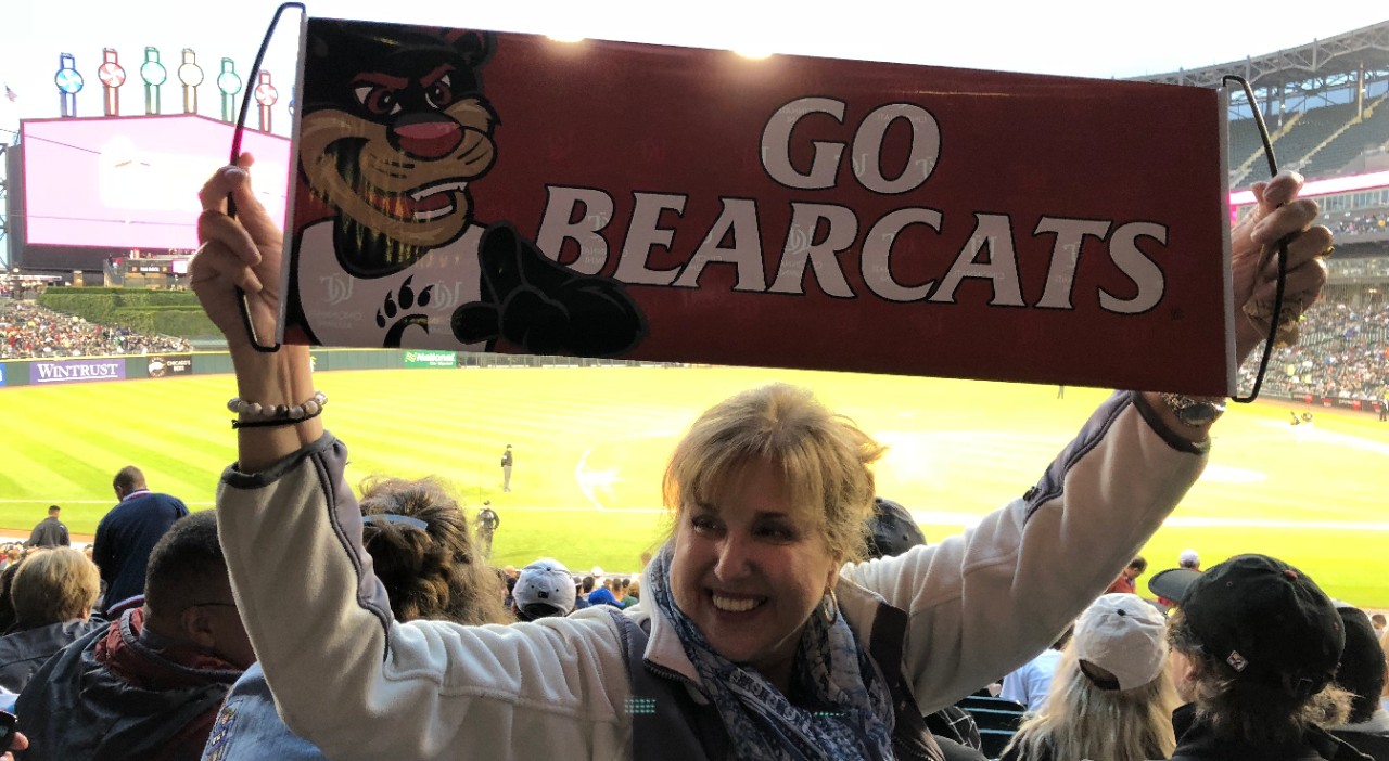 Woman sits in ballpark holding "Go Bearcats" sign
